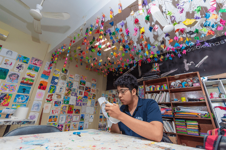 Alumno pinta en un salón de arte decorado con trabajos de colores